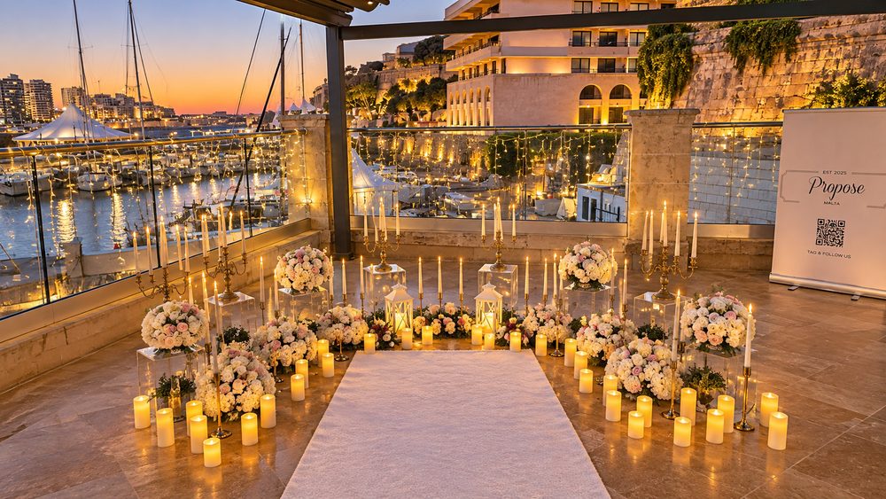 A candlelit aisle with white and pink flowers on a marina terrace at sunset