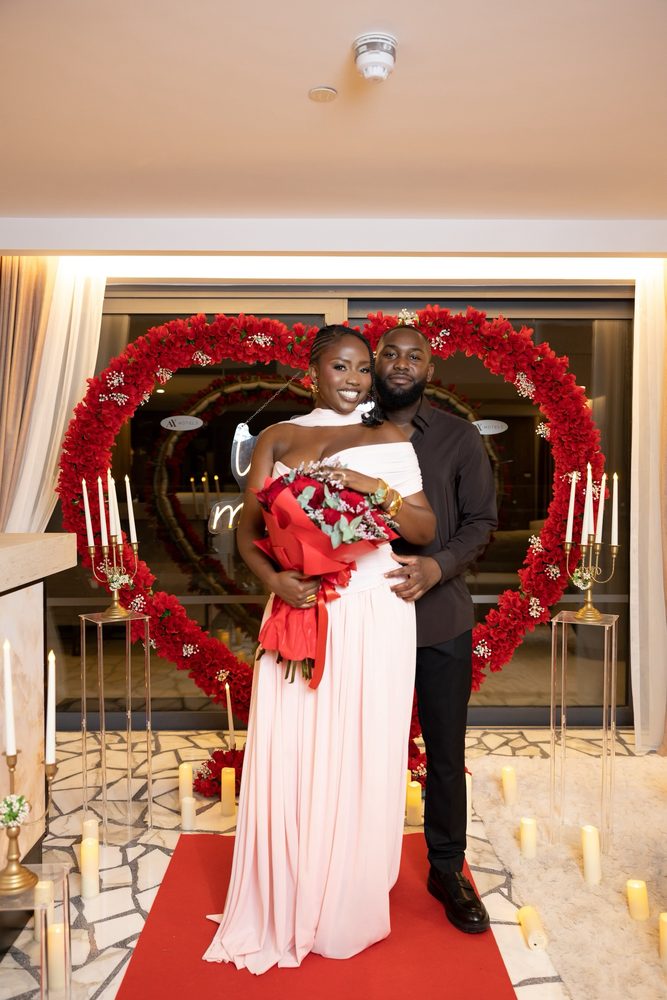 A couple with a red rose bouquet in front of the red heart arch