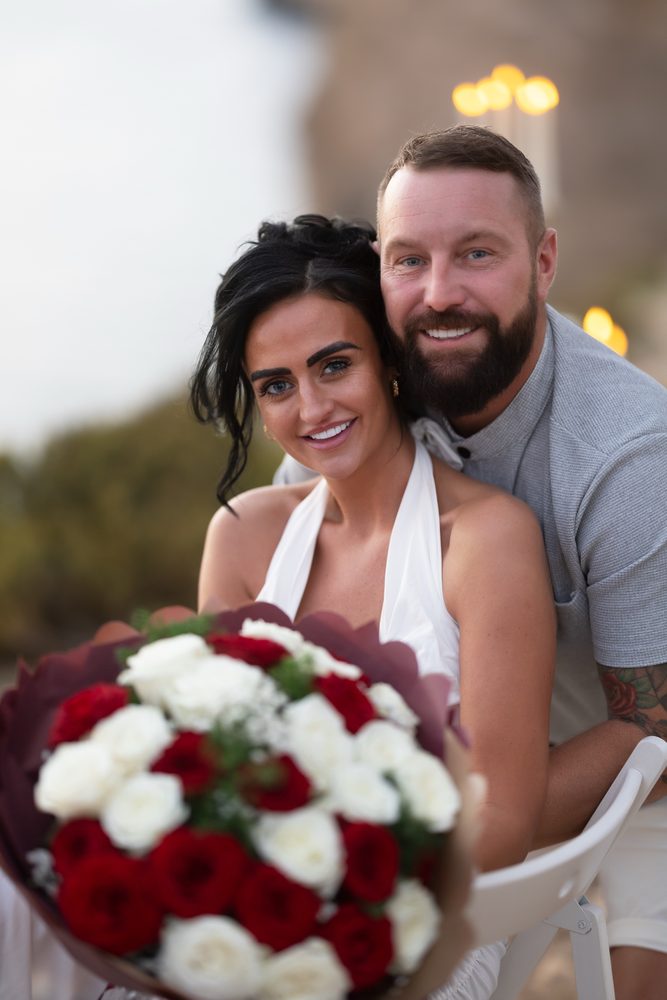 A couple with a red and white rose bouquet at dusk