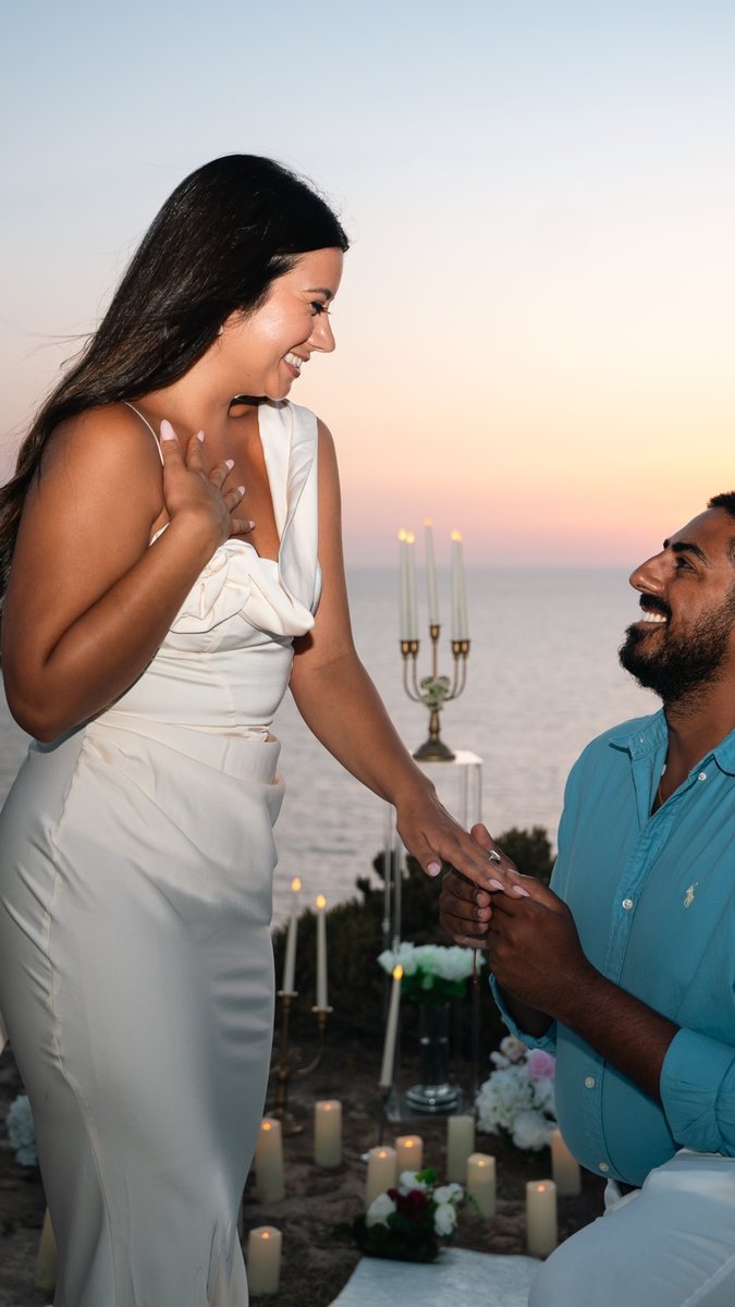 A man on one knee at sunset as his partner sees the ring